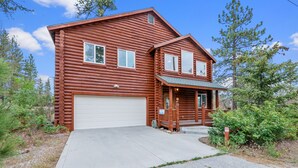 Une cabane en rondins à deux étages, dotée d’un garage, entourée d’arbres et sous un ciel dégagé.
