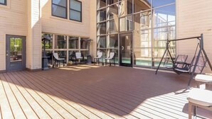 Une vaste terrasse extérieure dotée d’un plancher en bois, d’espaces aménagés pour s’asseoir et de grandes fenêtres offrant une vue sur les environs.