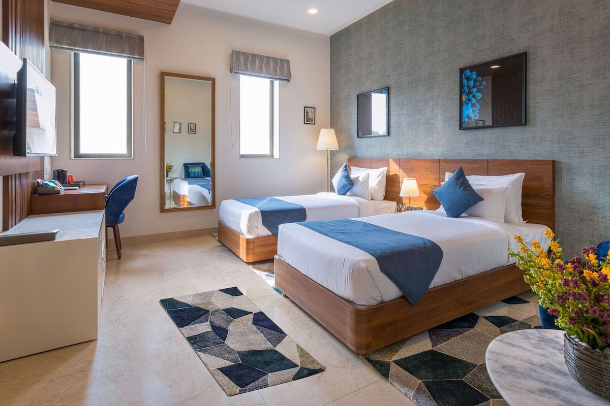 A hotel room with two beds, a desk, a chair, a mirror, and a large window.