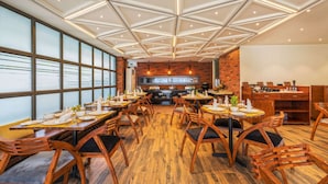 A restaurant with wooden tables and chairs, a brick wall, and a ceiling with geometric patterns. - Comfort Inn Dhaliwals Gurgaon (Gurugram)