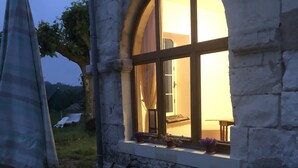 An outdoor seating area with a stone wall and a window with curtains.