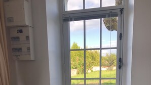 A room with a window seat overlooking a garden, a radiator below, and a black sofa to the left.