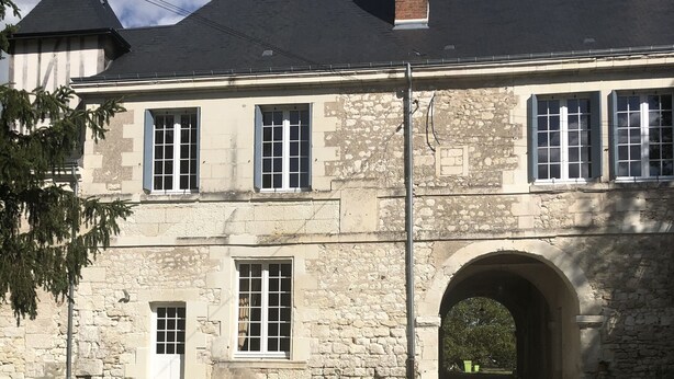 A stone building with a central archway, multiple windows, and a chimney.