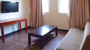 Ein Wohnzimmer mit einer Couch, einem Couchtisch aus Holz, einem an der Wand befestigten Fernseher und einem Fenster mit Vorhängen.