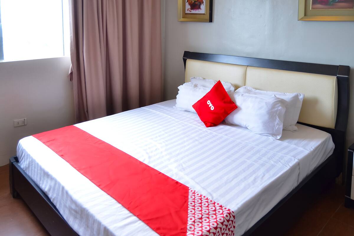 A neatly made bed with a red and white bedspread, a red pillow, and a white pillow.