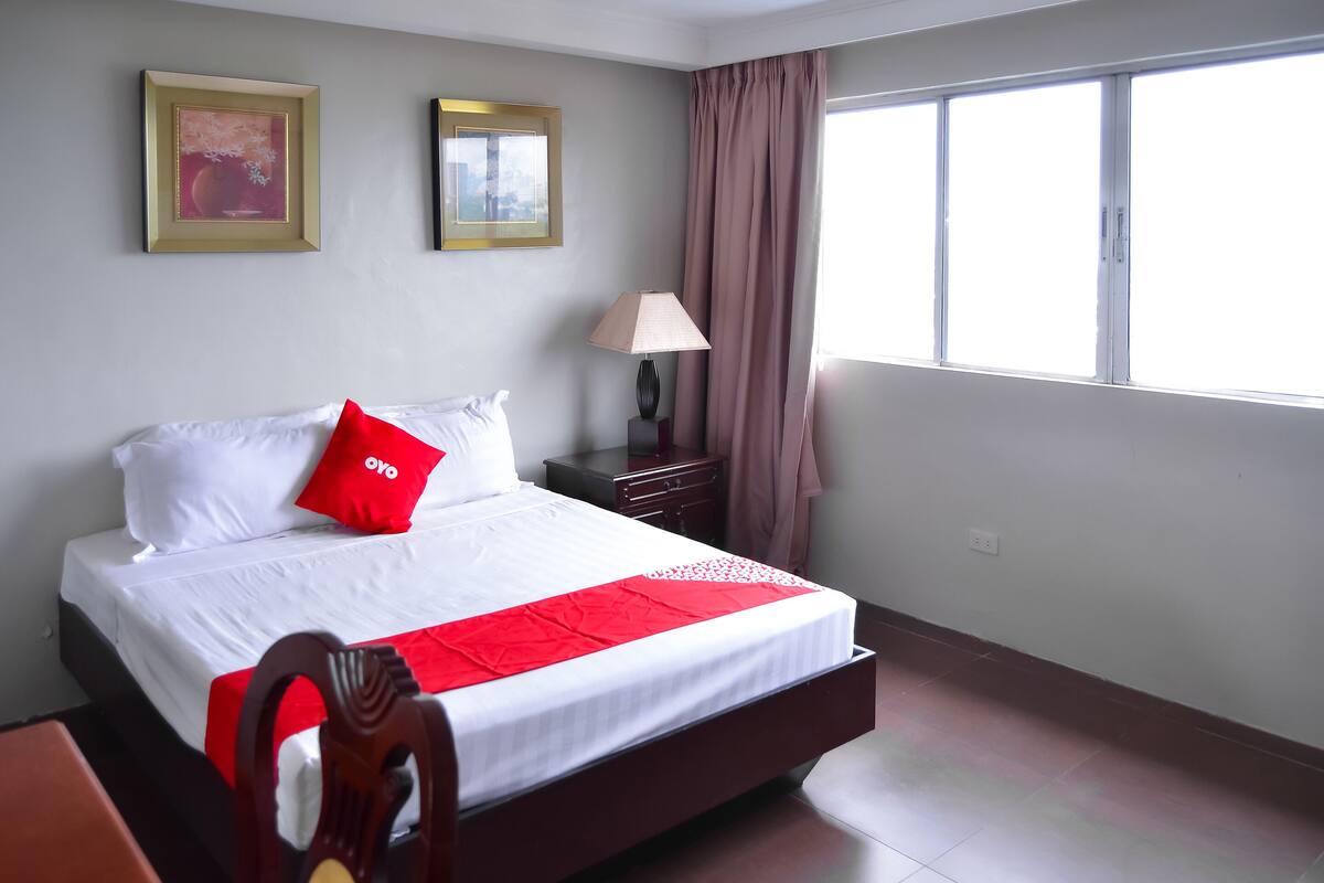 A hotel room with a bed, a nightstand, a lamp, and a window with curtains.
