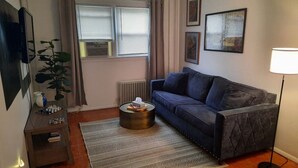A living room with a sofa, a coffee table, a plant, a radiator, and a lamp.