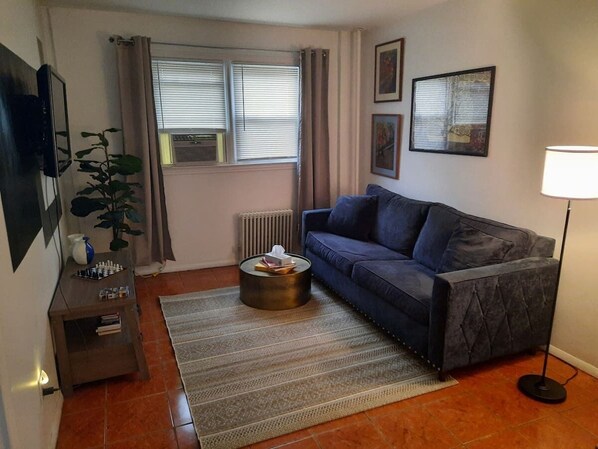 Una sala de estar con sofá, mesa de centro, planta, radiador y lámpara.