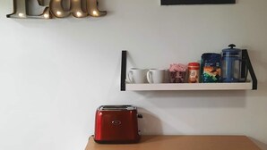 A kitchen with a toaster on the counter, a shelf with cups and coffee supplies, and a wall-mounted sign that reads "Eat".