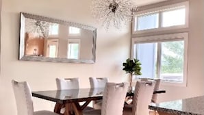 Een eetruimte met een houten tafel, beklede witte stoelen, een grote spiegel en een kroonluchter.