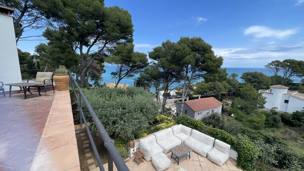 Eine Terrasse mit Gartenmöbeln, Blick aufs Meer und umgebender Bepflanzung.
