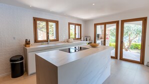 Eine moderne Küche mit einer großen Kochinsel, weißen Marmorarbeitsplatten, Holzschränken und großen Fenstern.