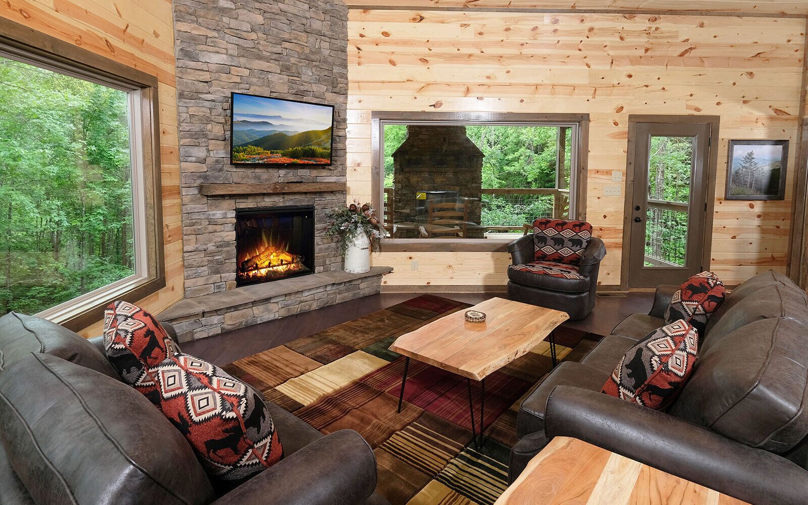 A cozy cabin interior with a stone fireplace, leather furniture, and large windows offering a view of the forest.