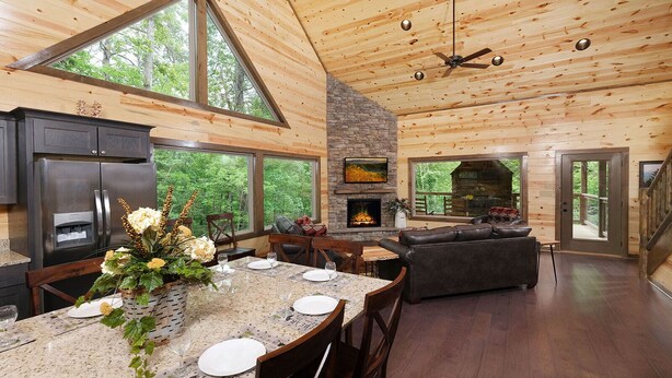 Un'ampia cucina con camino in pietra, soffitto in legno e ampie finestre con vista su una foresta.