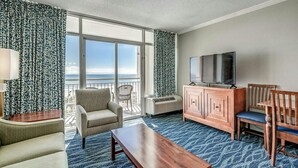 A hotel room with a large window, a television, a wooden cabinet, and a seating area with a chair and a sofa. - · Oceanfront Deluxe King. Indoor Waterpark, Pools and More (Myrtle Beach)