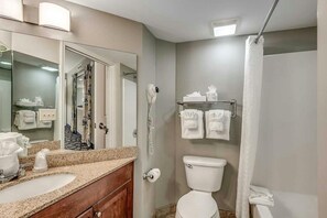 En-suite bathroom with sink, mirror, toilet, shower curtain, and towel rack.