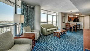 Une chambre d’hôtel avec une grande fenêtre, un canapé, un fauteuil, une petite table et une kitchenette.