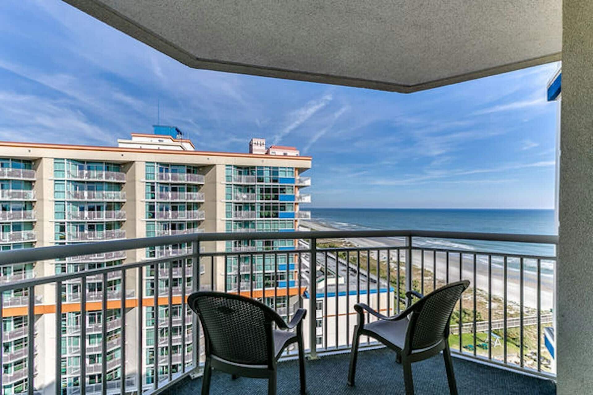 A balcony with two chairs overlooking a beach and a high-rise building.