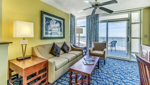 A room with a sofa, a coffee table, a lamp, a framed picture, and a ceiling fan. - · Angle Oceanfront 2 Bdrm. Multiple Pools, Great Location! (Myrtle Beach)