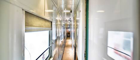 Un pasillo de tren con iluminación superior, ventanas y suelo de madera.