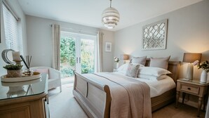 A bedroom with a bed, bedside tables, a dresser, and a window with curtains. - Bay Tree Cottage - Luxury Cottages (Cheltenham)