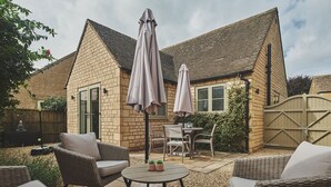 A patio area with wicker furniture, two umbrellas, and a table with potted plants. - Bay Tree Cottage - Luxury Cottages (Cheltenham)