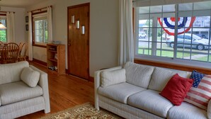 A living room with a sofa, armchair, wooden floor, and a window with curtains. - Visit our charming cottage this Fall & Winter. Enjoy the Scenery & Ski Slopes. (McKnightstown)