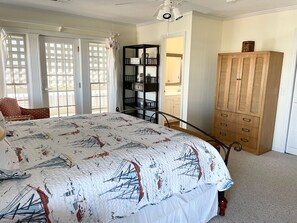 A bedroom with a large bed, a wooden wardrobe, a bookshelf, and a view through a window with a white curtain. - "A Captains Cottage" oceanfront 4 bedroom, 3 bathroom (Holden Beach)