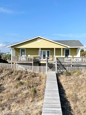 A yellow house with a wooden deck and a wooden walkway leading to the front door. - "A Captains Cottage" oceanfront 4 bedroom, 3 bathroom (Holden Beach)