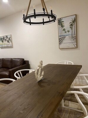 A dining area with a wooden table, white chairs, a chandelier, and artwork on the walls. - PARADISE FOUND! (Key Largo, FL 33037)
