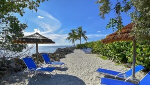A beach with blue lounge chairs, a thatched umbrella, and a view of the ocean. - PARADISE FOUND! (Key Largo, FL 33037)
