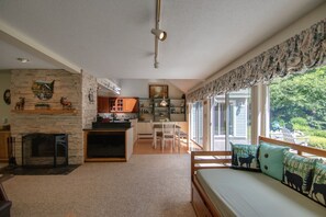 Cozy living area with a fireplace, sofa, and dining table, offering a view of the outdoors through large windows.