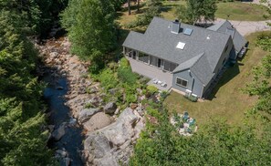 A modern house with a large deck, a river nearby, and a well-maintained garden. - Picturesque Ski getaway close to Loon Mountain and Waterville Valley Ski Resorts (Thornton)