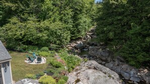 A deck with outdoor furniture, a small garden area with plants, and a rocky stream. - Picturesque Ski getaway close to Loon Mountain and Waterville Valley Ski Resorts (Thornton)
