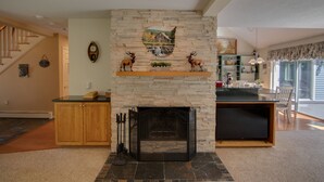 A living room with a stone fireplace, wooden cabinets, and a staircase leading to another level. - Picturesque Ski getaway close to Loon Mountain and Waterville Valley Ski Resorts (Thornton)