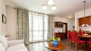 Una sala de estar con un sofá, una mesa de comedor con sillas y una zona de cocina con armarios y una lámpara colgante.