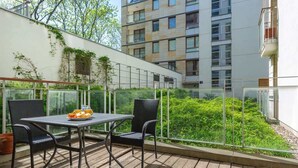 Un balcón con una mesa y sillas, con vistas a un jardín y un edificio.