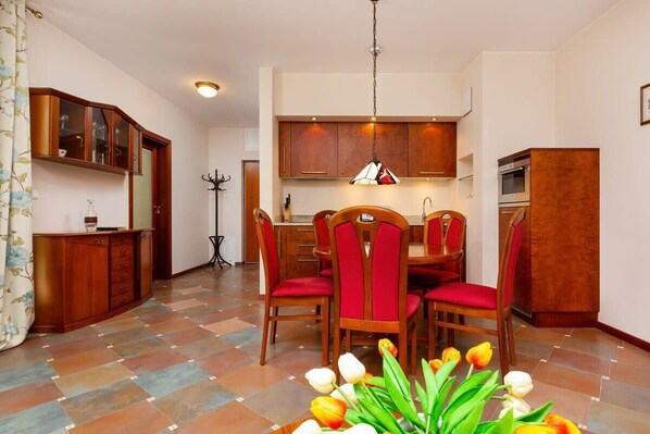 A dining area with a wooden table and red upholstered chairs, a kitchen with wooden cabinets, and a tiled floor.