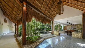 A spacious indoor area with a thatched roof, a stone wall, and a patterned floor. - Casa del Jaguar Beach Hotel (Isla Mujeres)
