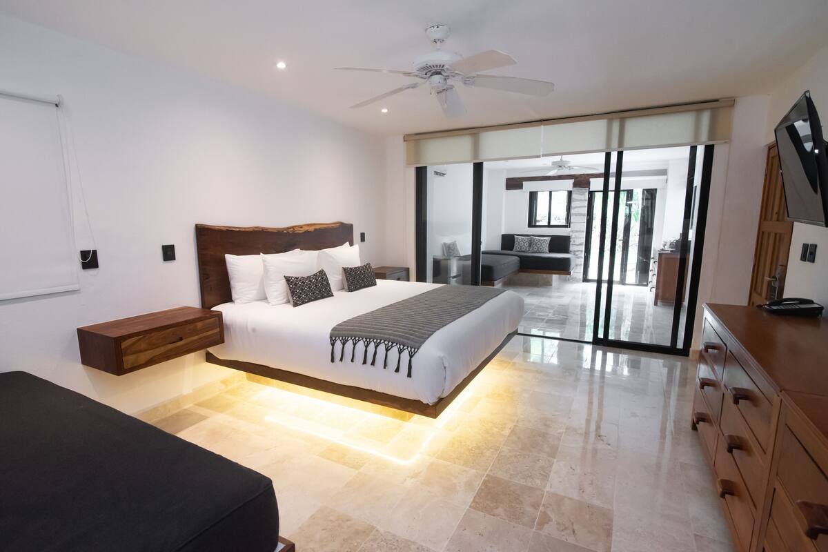 A modern bedroom with a large bed, a bedside table, a wardrobe, and a sliding glass door leading to a balcony.