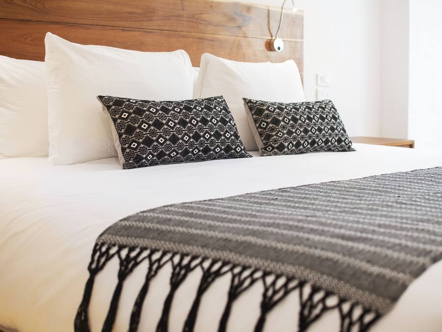 Ein ordentlich bezogenes Bett mit weißen und gemusterten Kissen, einer grauen Decke mit Baummotiven und einem hölzernen Kopfteil.