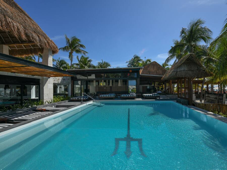 A swimming pool with lounge chairs, a thatched-roof structure, and palm trees.