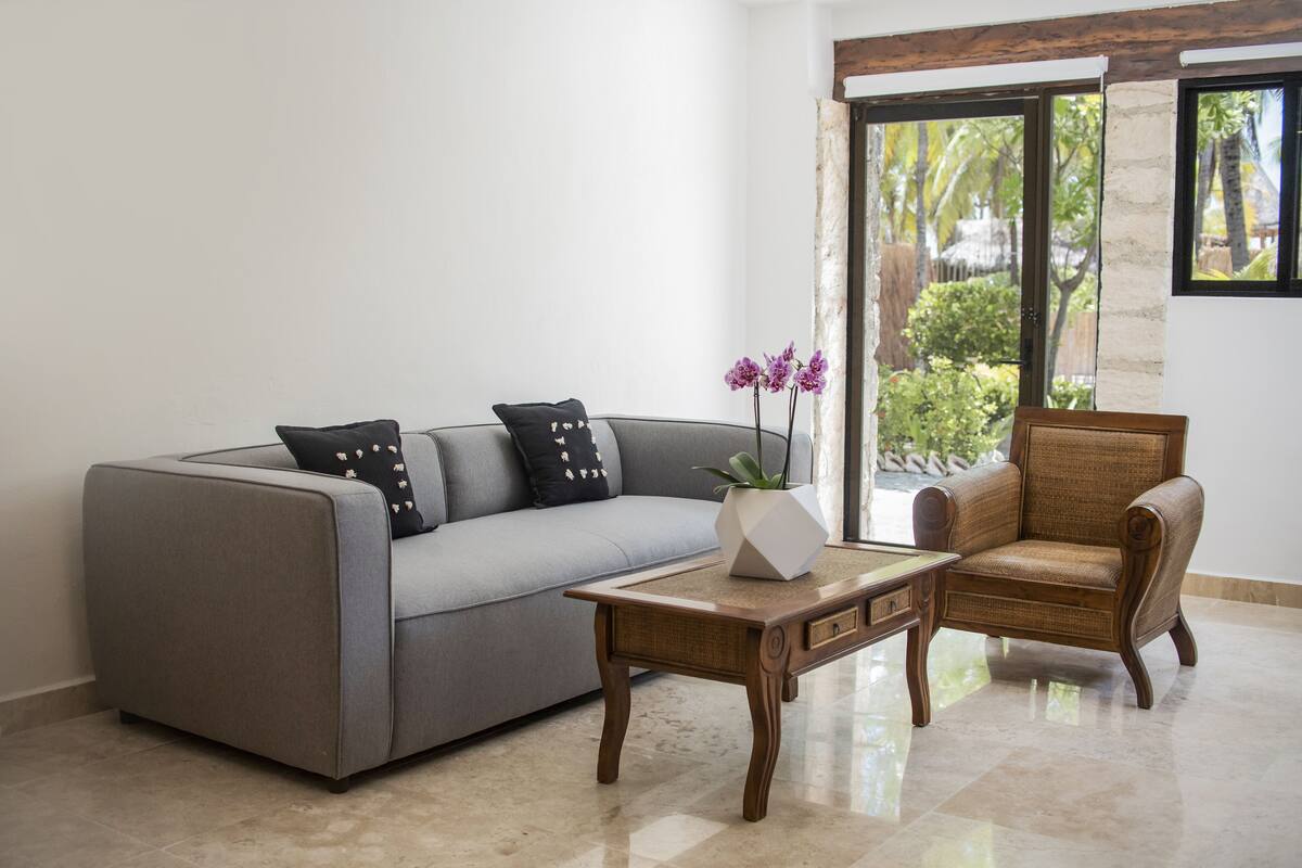 A living room with a grey sofa, a wooden coffee table, and a wicker armchair.