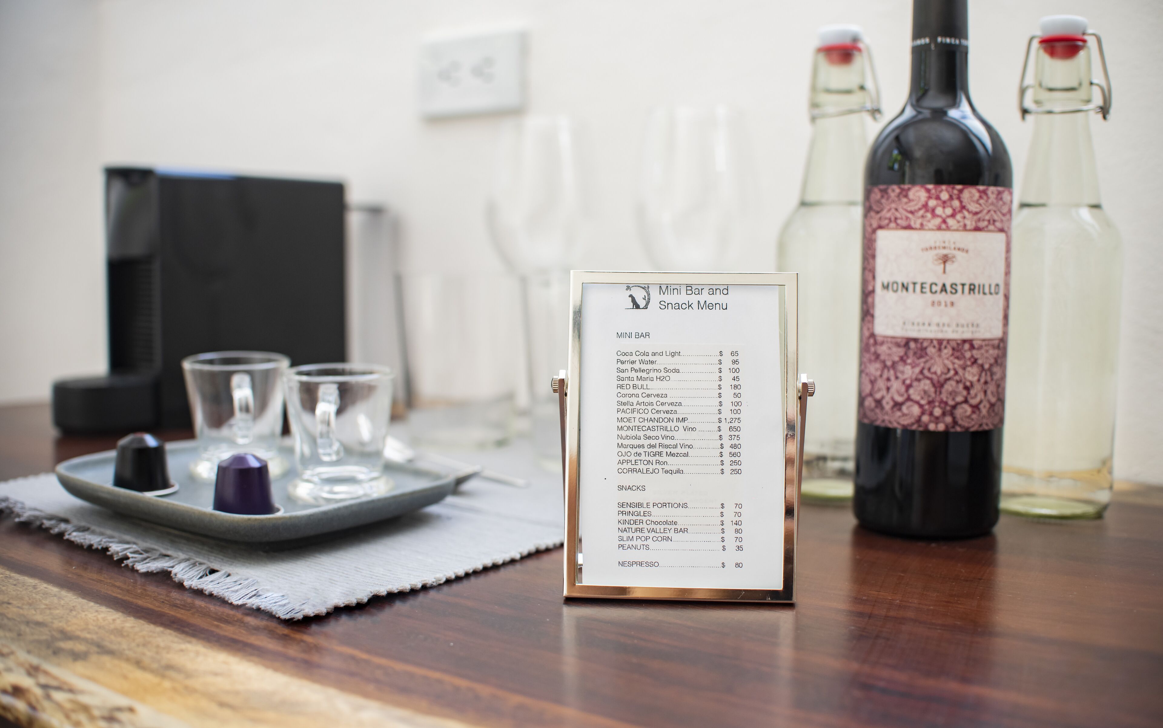 Un panneau affichant les prix des boissons et des en-cas, une bouteille de vin et des verres sur une table.