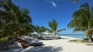 A beach with white sand, palm trees, and lounge chairs with umbrellas. - Casa del Jaguar Beach Hotel (Isla Mujeres)