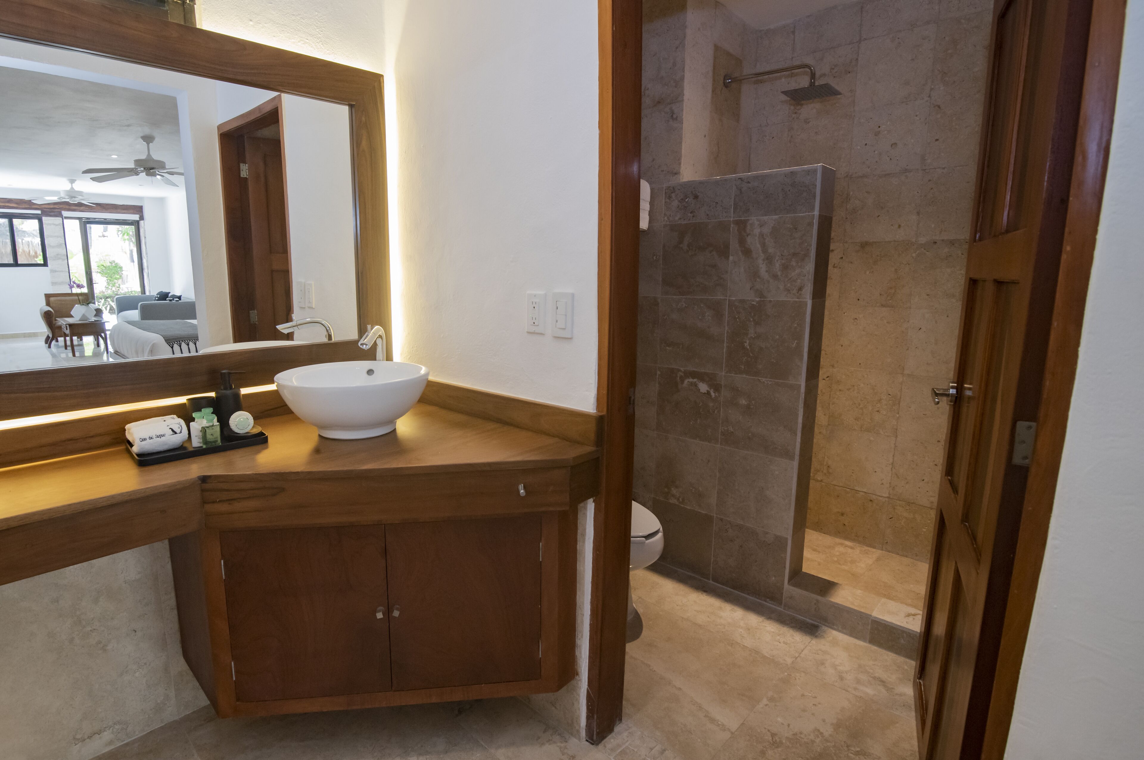 Un baño con tocador de madera, lavamanos blanco y ducha con cerramiento de vidrio.