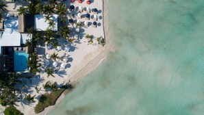 An aerial view of a beach resort with a pool, sun loungers, umbrellas, and palm trees. - Casa del Jaguar Beach Hotel (Isla Mujeres)