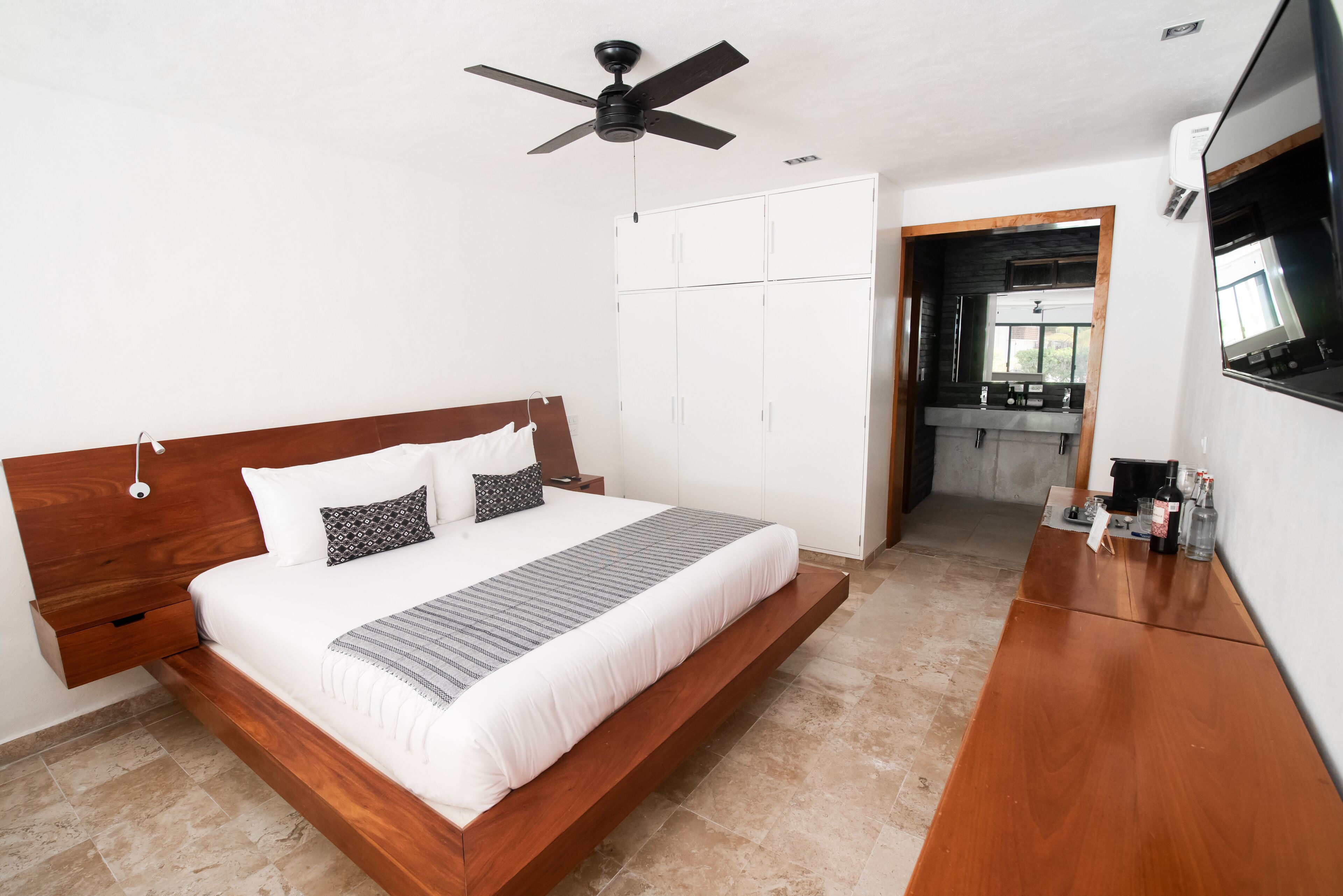 A modern bedroom with a wooden bed, white wardrobe, and a kitchenette area.