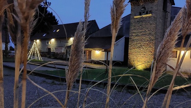 A stone building with a sloped roof, surrounded by tall grasses and a gravel path.