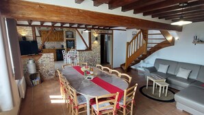 A dining area with a wooden table and chairs, a kitchen in the background, and a staircase leading upstairs.